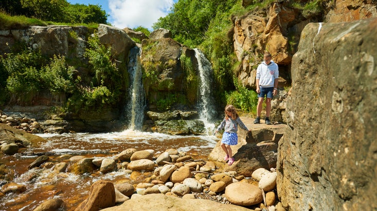 A boy and a girl making their way down the rocks to bottom of small waterfall